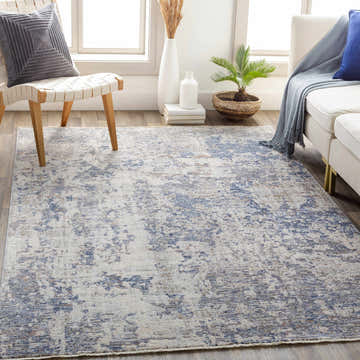 Living room scene with Broxbourne Area Rug in denim, taupe, and cream colors, styled with a white sofa and modern chair. Roomscene-Rectangle