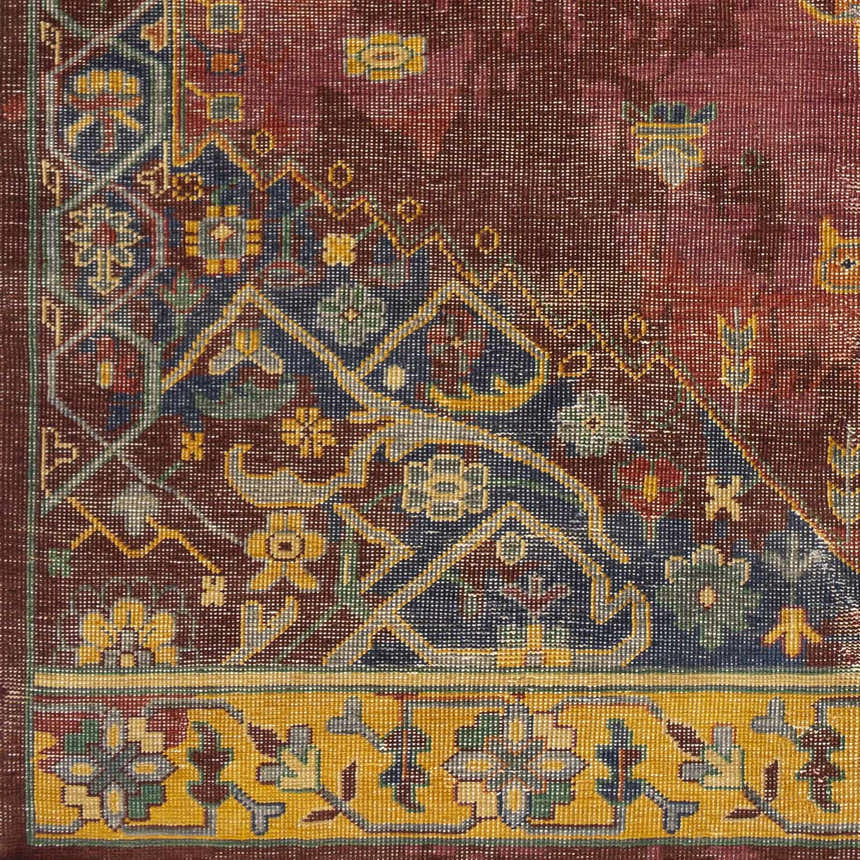 Close-up of the Brush Premium Handmade Wool Rug. Features brick red, blue, and mustard floral and geometric patterns. Swatch
