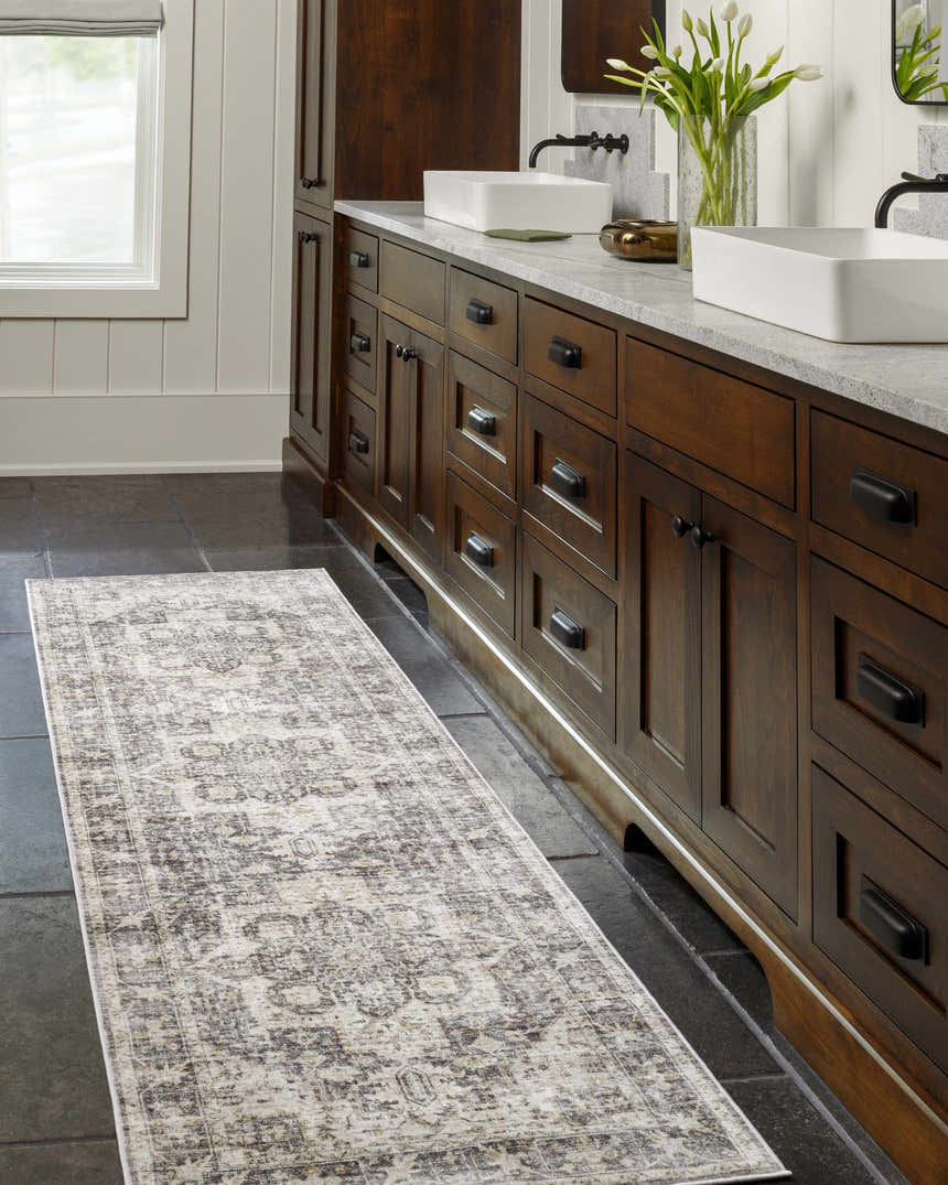 Bathroom scene with a gray and taupe Bevin Washable Area Rug runner in front of a dark wood vanity with white sinks. Roomscene-Runner