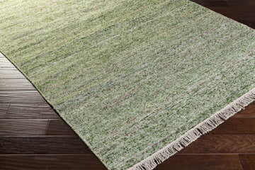 Close-up of a green Campti Area Carpet with ivory fringe on dark wood floors. Wool and viscose contemporary rug. Corner