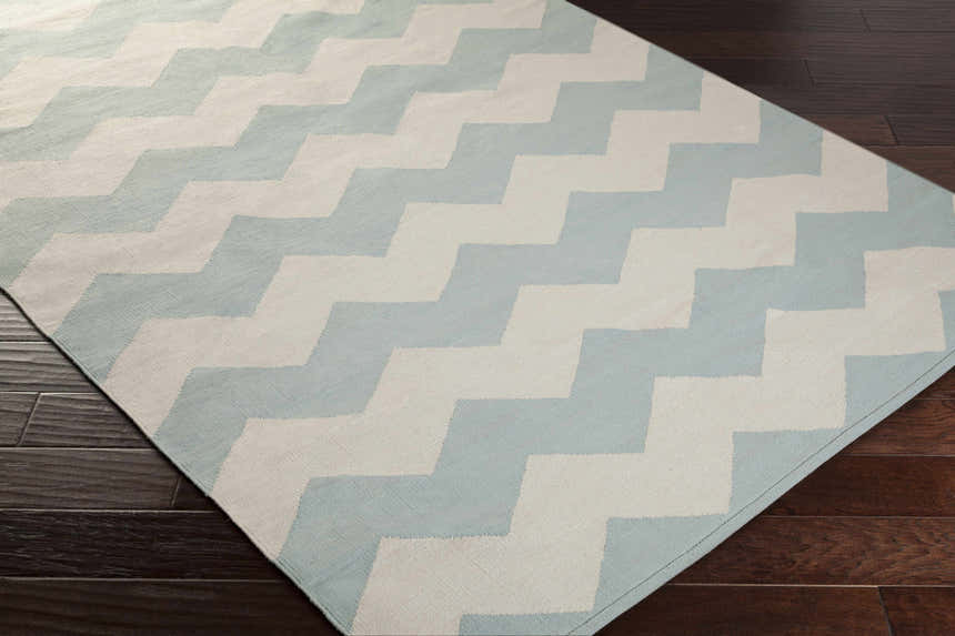 Close-up of the Caswell Area Rug in ice blue and ivory chevron pattern on dark wood floors. Hand woven cotton rug. Corner