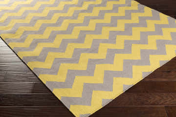 Close-up of the Cedarcreek Area Rug. Hand-woven wool rug with a gray and mustard yellow chevron pattern. Corner