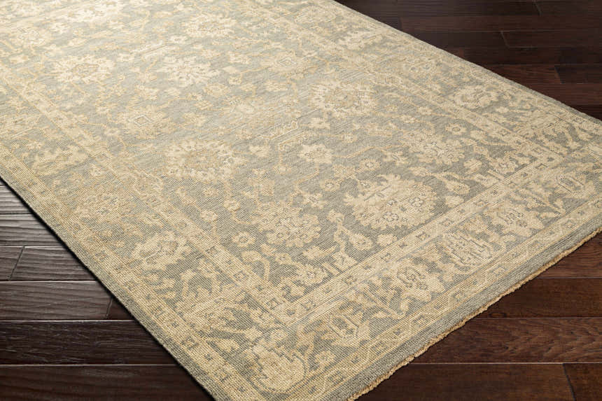 Close-up of the hand-knotted Chalgrove Area Rug in beige and dusty sage with a traditional floral pattern on dark wood floors. Corner