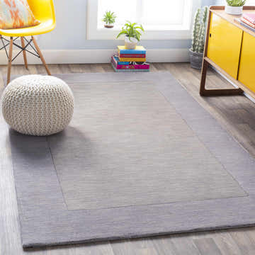 Living room scene with a Bordered Solid Gray Wool Rug, yellow chair, white pouf, and yellow cabinet. Roomscene-Rectangle