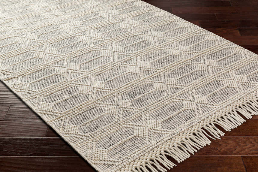 Close up of the Chars Wool Rug with tassels, bone color, geometric pattern, on dark wood floor. Corner