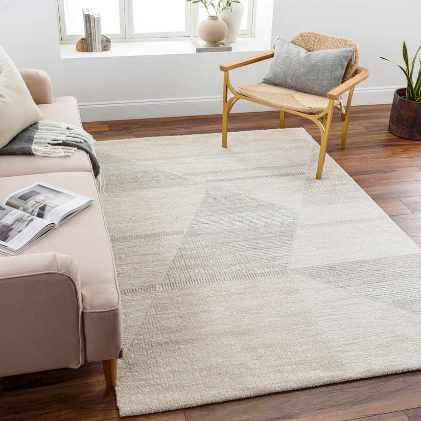 Living room with Chizu Geometric Neutral Luxe Rug, a bone-colored sofa, and a woven chair on a dark wood floor. Roomscene-Rectangle