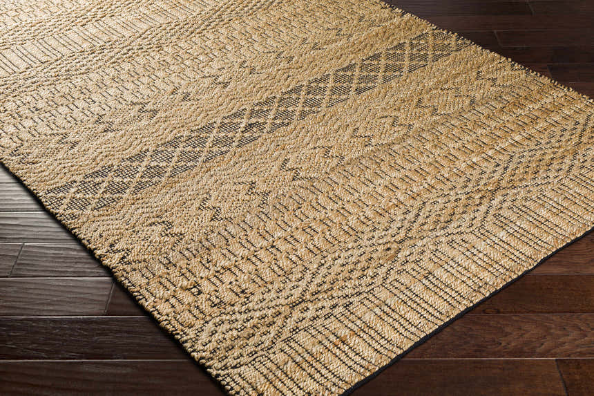 Close up of a Cloverly Tribal Jute Carpet. Tan jute rug with black tribal-inspired geometric patterns and woven texture. Corner