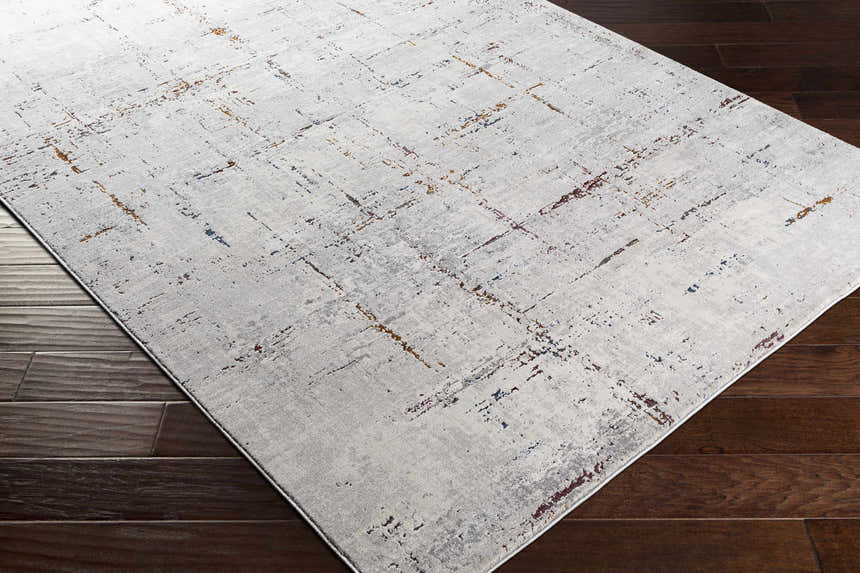 Close-up of a Concordia Faux Silk Rug. Abstract design in off-white, gray, burgundy, burnt orange, and navy on dark wood floors. Corner
