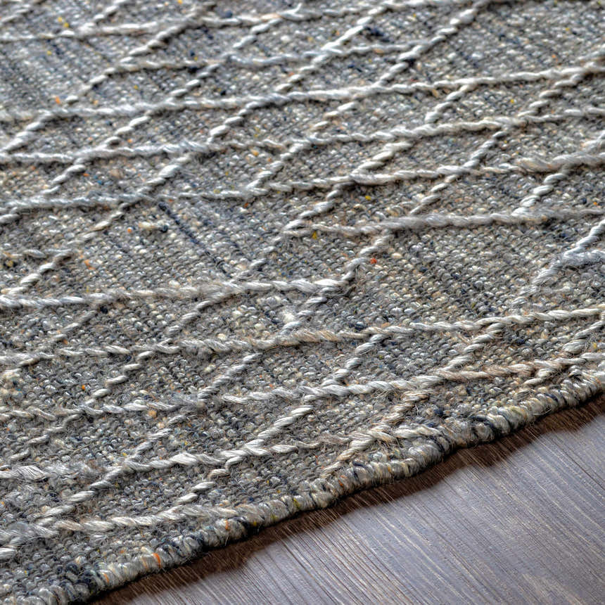 Close-up of the Colinton Area Rug showing its hand woven texture, gray tones, and geometric pattern on a wood floor. Texture