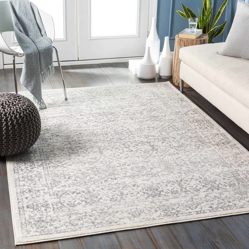 Living room scene with a charcoal and off white Comstock Area Rug, sofa, chair, and gray pouf. Roomscene-Rectangle