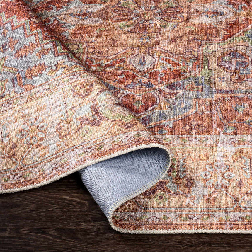 Close-up of the Casterton Washable Area Rug showing the brown, burnt orange, and denim traditional pattern and woven texture. Fold