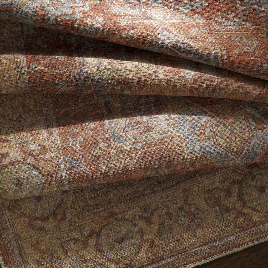 Close-up of folded Casterton Washable Area Rug. Bohemian style rug with brown, orange, green, and beige traditional pattern. Fold