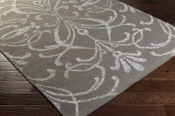 Close-up of the Cottekill Area Rug. Brown wool rug with an off-white, contemporary floral pattern on dark wood floors. Corner