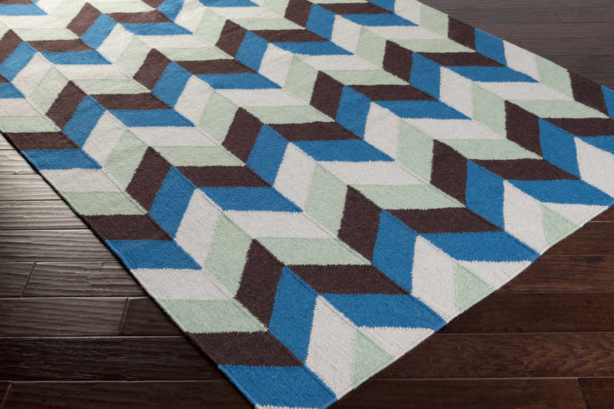 Close-up of the Curtin Carpet. Hand woven wool rug with blue, sage, white, and navy geometric pattern on a wood floor. Corner