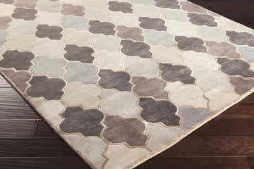 Close-up of the hand-knotted Cuero Area Rug. Charcoal, light brown, and taupe quatrefoil pattern on dark wood floor. Corner