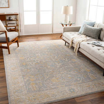 Living room scene with a Dally Thick Luxe Statement Rug in charcoal, gray, and mustard tones. Farmhouse style with sofa, chair, and wood floors. Roomscene-Rectangle