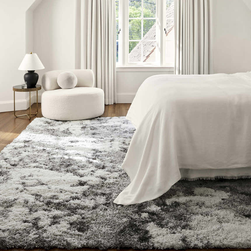 Bedroom scene with a gray and white Dawesville shag rug, white bed linens, and a modern white chair near a window. Roomscene-Rectangle
