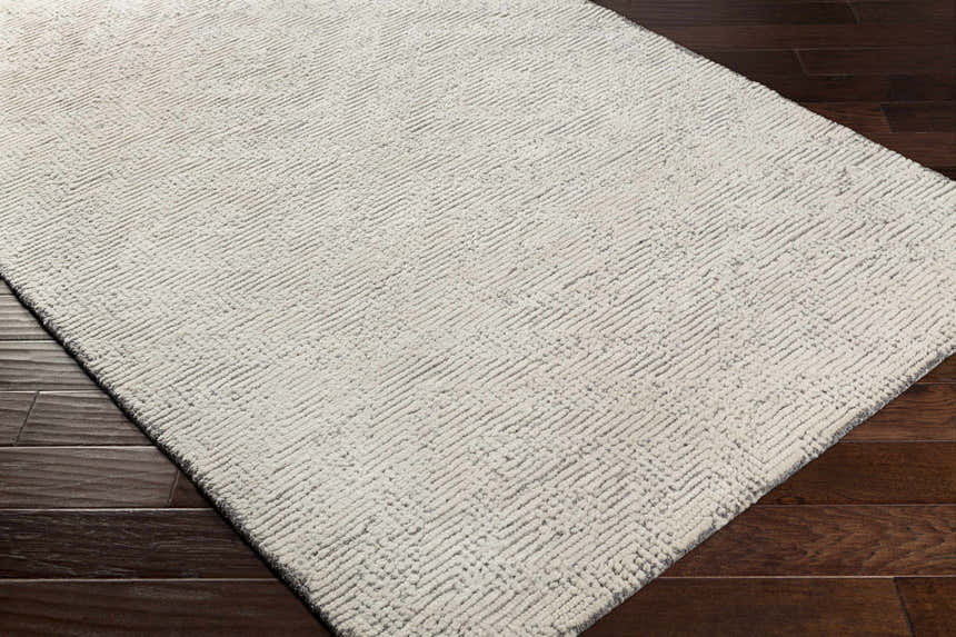 Close-up of the hand-tufted Delahey Area Rug. Cream and charcoal wool rug with a subtle geometric pattern. Corner