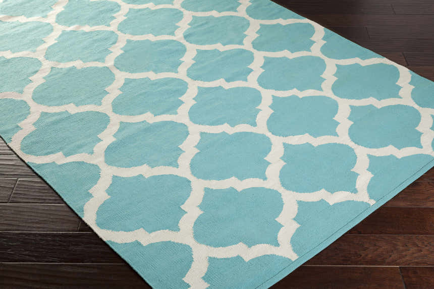 Close-up of the Derry Area Rug. Aqua cotton rug with an ivory quatrefoil pattern on a dark wood floor. Corner