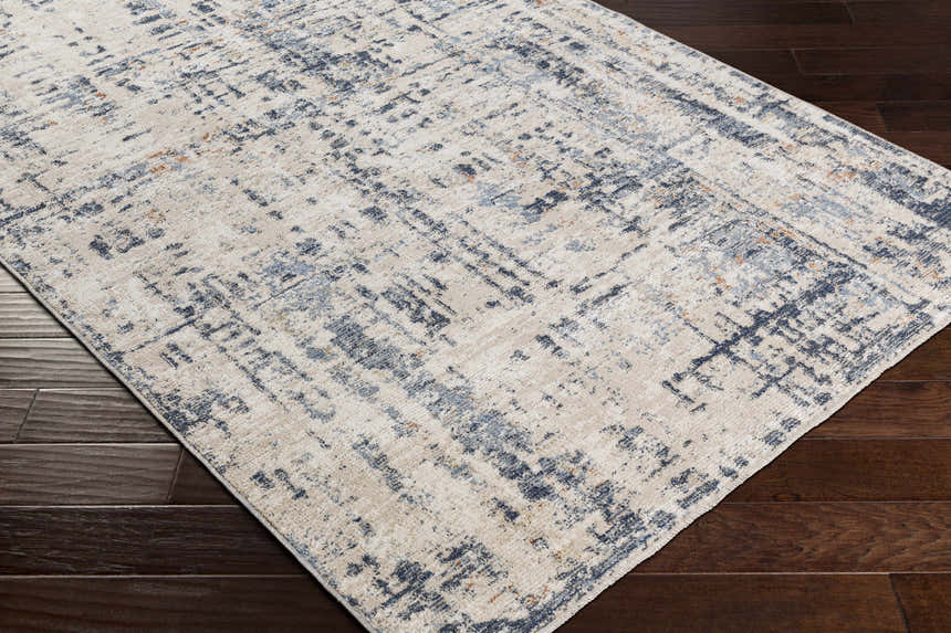 Close-up of the Dalama Area Rug, a contemporary design in dark gray, ivory, and navy on a dark wood floor. Corner