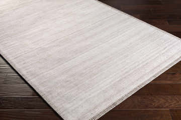 Close-up of the hand-woven Denison Viscose Area Carpet in cream, medium gray, and oatmeal on a dark wood floor. Corner