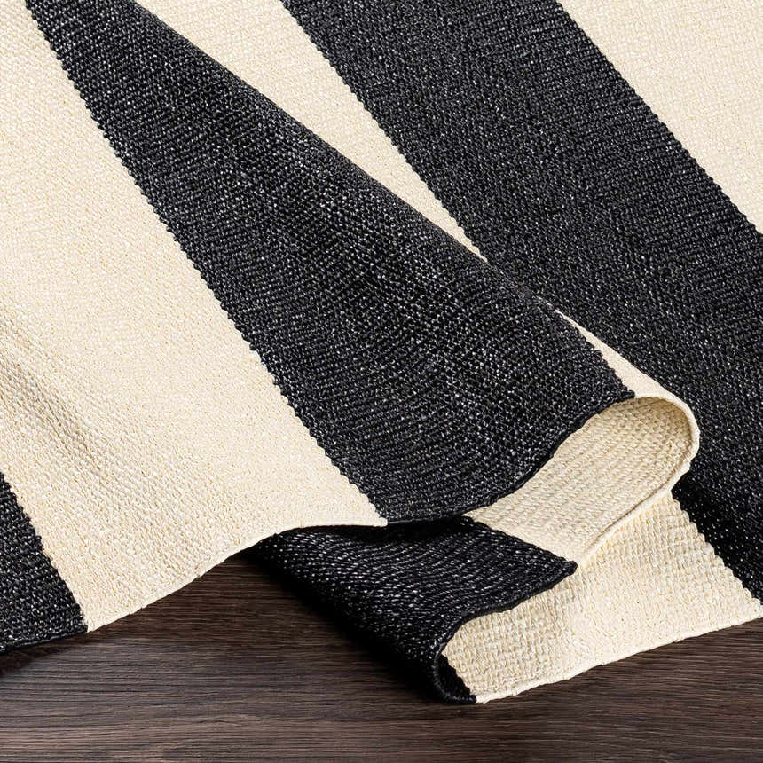 Close-up of the Douds Area Rug. Hand-woven PVC rug with bold black and cream stripes. Contemporary style. Fold