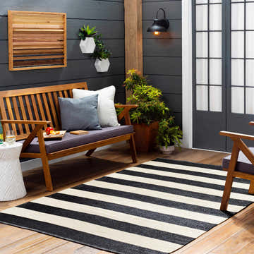Outdoor patio scene with a black and cream striped Douds Area Rug, wooden bench, and dark gray wall. Roomscene-Rectangle