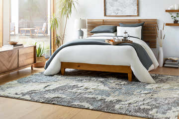 Bedroom scene with a Doveton Plush Wool Rug in black, blue, and cream under a wooden bed frame. Modern, bright, and airy. Roomscene-Rectangle
