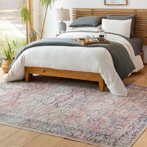 Bedroom scene with a Dunsha Boutique Washable Area Rug in blue, coral, and pink tones under a wooden bed frame. Roomscene-Rectangle