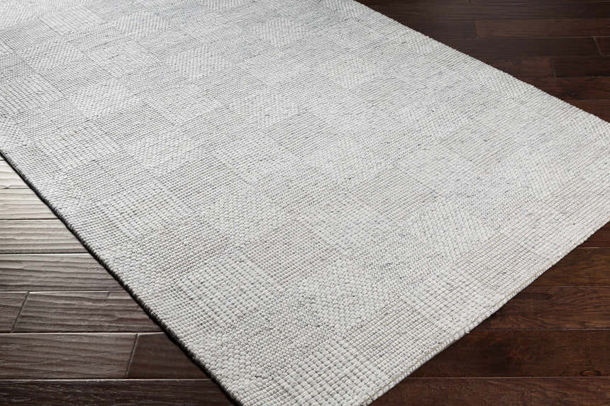 Close up of Eckman Wool Checkered Rug in off white, charcoal and black on dark wood floor. Hand woven texture. Corner