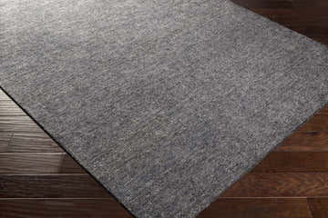 Close-up of the textured Lecompton Solid Charcoal Viscose Rug on dark hardwood flooring. Contemporary style. Corner