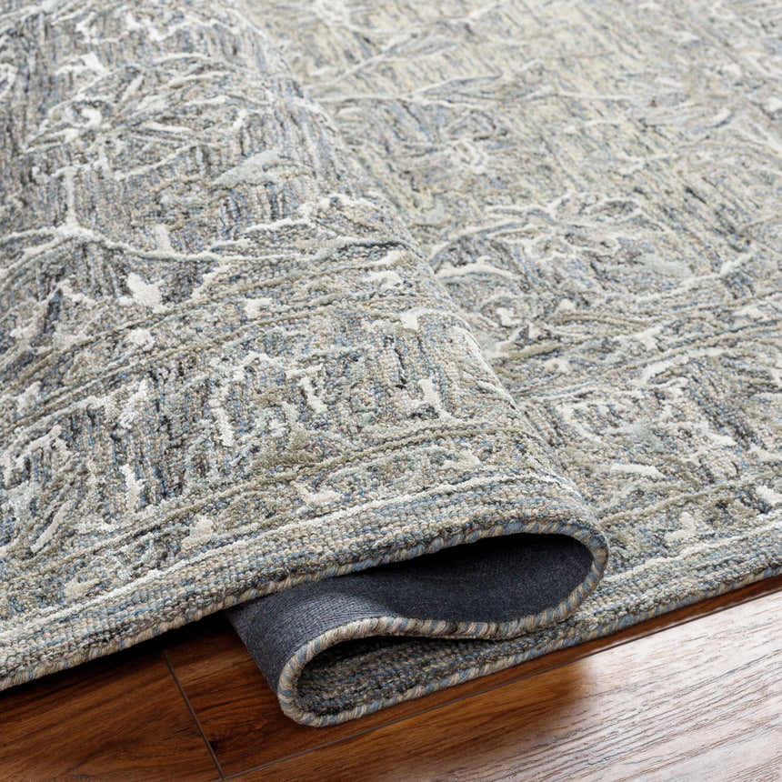 Close-up of the Eriline Wool & Faux Silk Rug. Features a denim, ivory, and sage traditional pattern with a hand-tufted texture. Fold