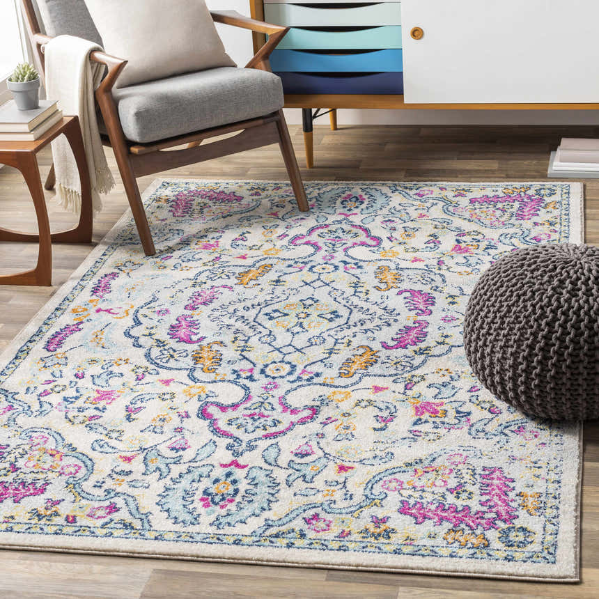 Living room scene with Errol Area Rug. Bohemian rug in aqua, pink, and yellow under gray chair and pouf. Roomscene-Rectangle