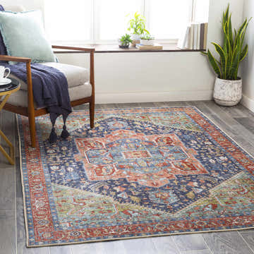Living room scene with Exira Washable Area Rug in blue, brick red, and camel colors. Bohemian style rug under chair. Roomscene-Rectangle