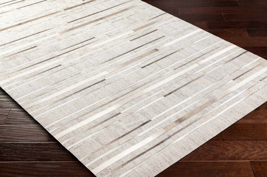 Close-up of the Fico Area Rug showing its ivory, tan, and taupe geometric pattern on dark brown wood floors. Corner