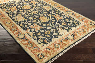 Close-up of a hand-knotted Fielding Area Carpet. Farmhouse style rug in black, brown, burnt orange and tan on dark wood floor. Corner