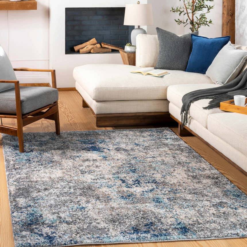 Living room scene with a Findochty Blue&Gray Abstract Area Rug, cream sectional, gray chair, and fireplace. Roomscene-Rectangle