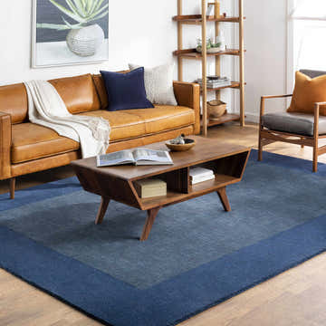 Living room with a brown leather sofa and Bordered Solid Ink Blue Wool Rug. Roomscene-Rectangle