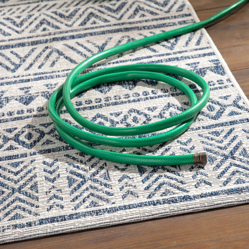 Close-up of the Novato Navy All Over Pattern Performance Rug with a blue and white geometric design and a green garden hose. Styleshot