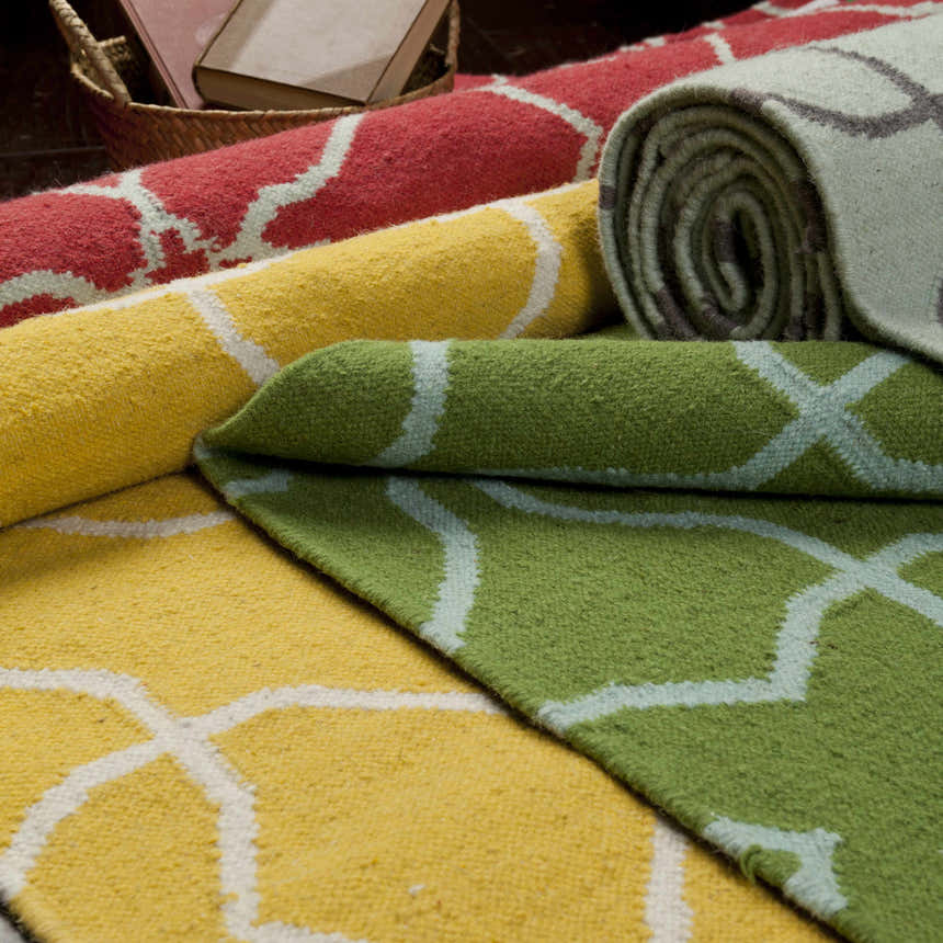 Close-up of rolled Creekside Area Rugs. Hand-woven wool rugs in red, yellow, green, and gray with a geometric pattern. Styleshot