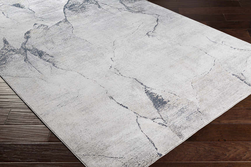 Close-up of the Gasquet Gray Marble Textured Luxe Rug showing charcoal and light gray marbled design on dark wood floor. Corner