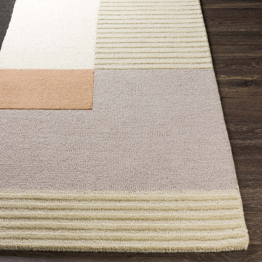 Close-up of the Glenmavis Area Rug. Geometric design in black, beige, gray, peach, and tan wool on a wood floor. Front
