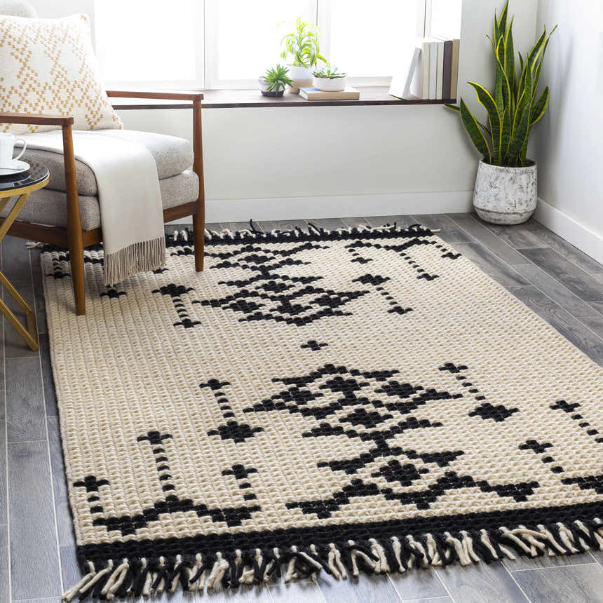 Living room scene with a Glenorie Area Rug. Black and cream wool rug with bohemian pattern, chair, and plants. Roomscene-Rectangle