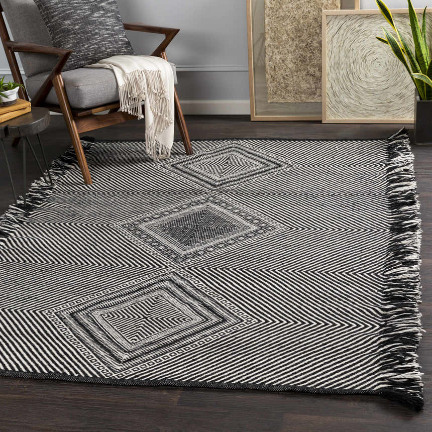 Living room scene with Eaglesham Black&White wool rug. Bohemian style, geometric pattern, tassel fringe. Gray chair, wood floors. Roomscene-Rectangle