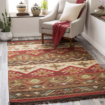 Living room scene with a Grimsby Wool Area Rug in burgundy, brown, and beige under a gray chair with a red throw. Roomscene-Rectangle