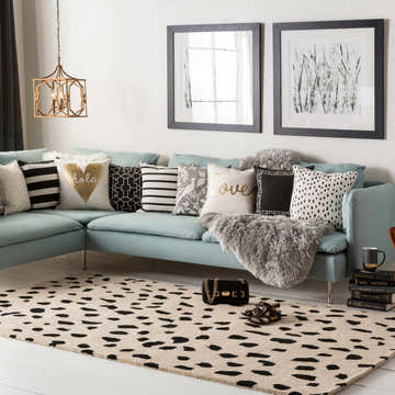 Living room scene with a Guiseley Dalmatian rug, blue sofa, patterned pillows, and black and white framed art. Roomscene-Rectangle