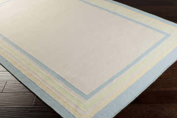 Close-up of the hand woven Hackberry Area Rug. Ivory wool rug with light blue, olive, and yellow border stripes. Corner