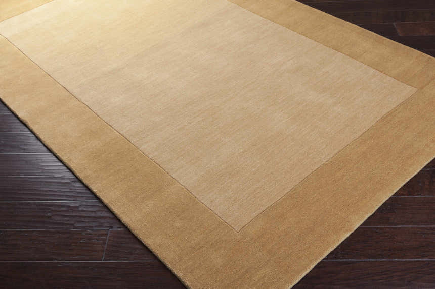 Close-up of a Bordered Solid Camel Yellow Wool Rug showing its texture and color on dark wood flooring. Corner