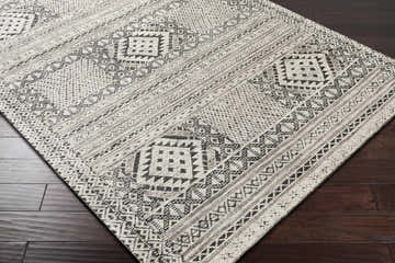 Close-up of Hemyock Premium Wool&Viscose Carpet. Black, charcoal, and off-white bohemian pattern on dark wood floor. Corner