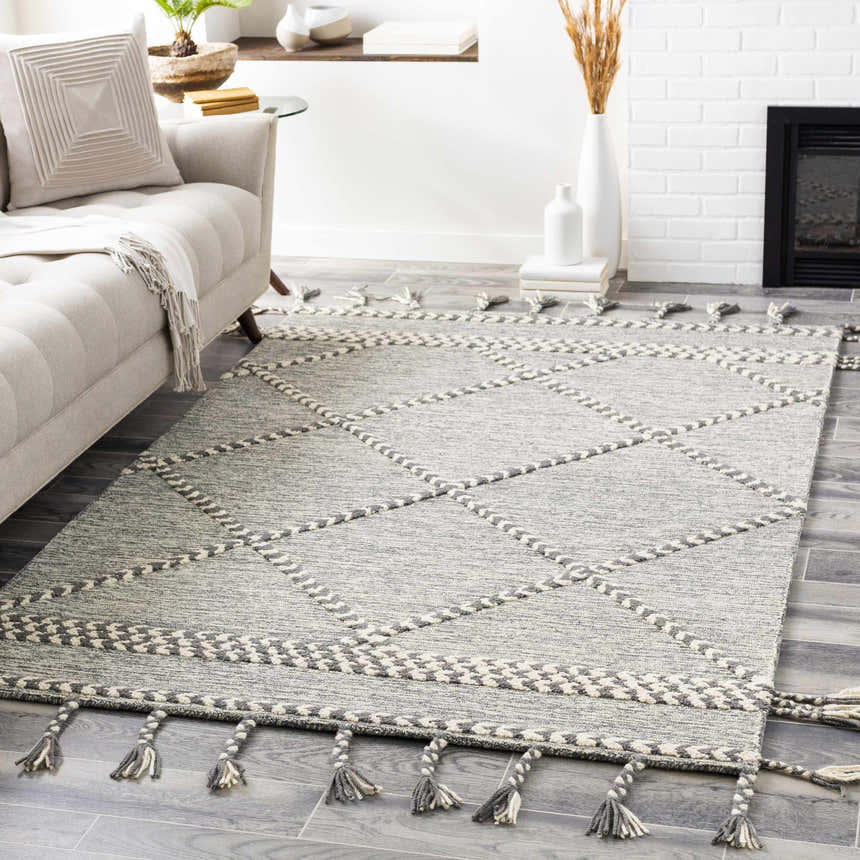 Living room scene with Hertfordshire Gray Trellis Tassel Wool Rug, sofa, fireplace, and gray wood floors. Roomscene-Rectangle